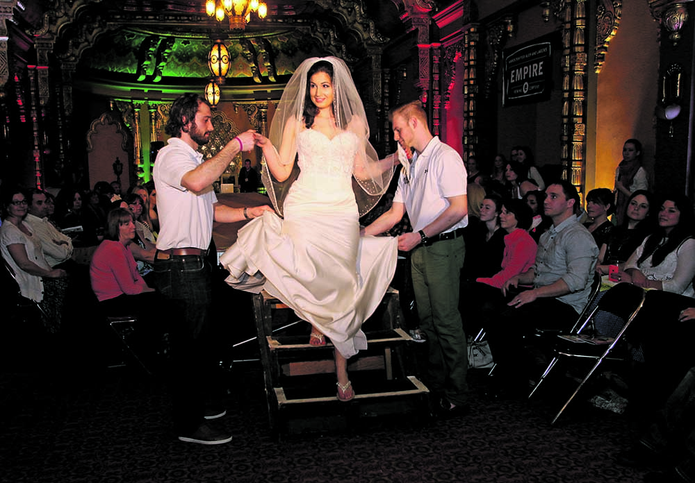 A model wearing a bridal gown from Spybaby is helped down from the runway during Syracuse Fashion Week's Opening Night Gala Wednesday at the Landmark Theater.