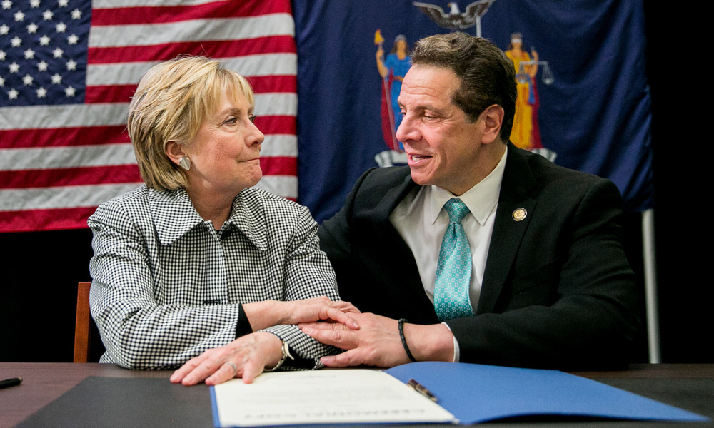 Hilary Clinton and Andrew Cuomo sit at a table together speaking.