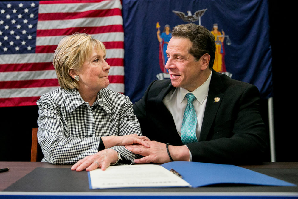 Hilary Clinton and Andrew Cuomo sit at a table together speaking.