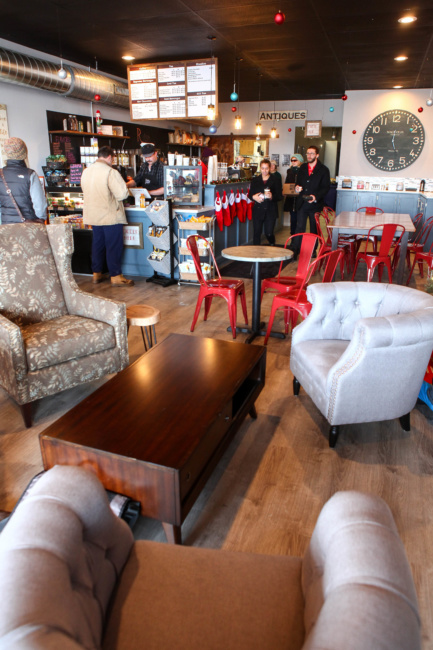 A shot inside Rise & Grind Cafe in Camillus. Armchairs sit around a coffee table in the foreground, while smaller tables with red metal chairs are further back.