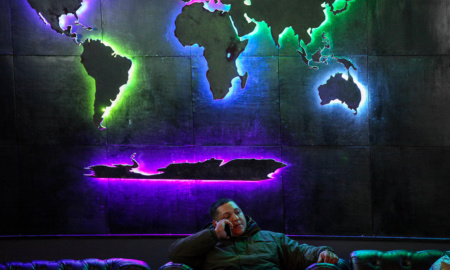 A man sits in Orbis Lounge, under a backlit wall display showing each continent in a world map.
