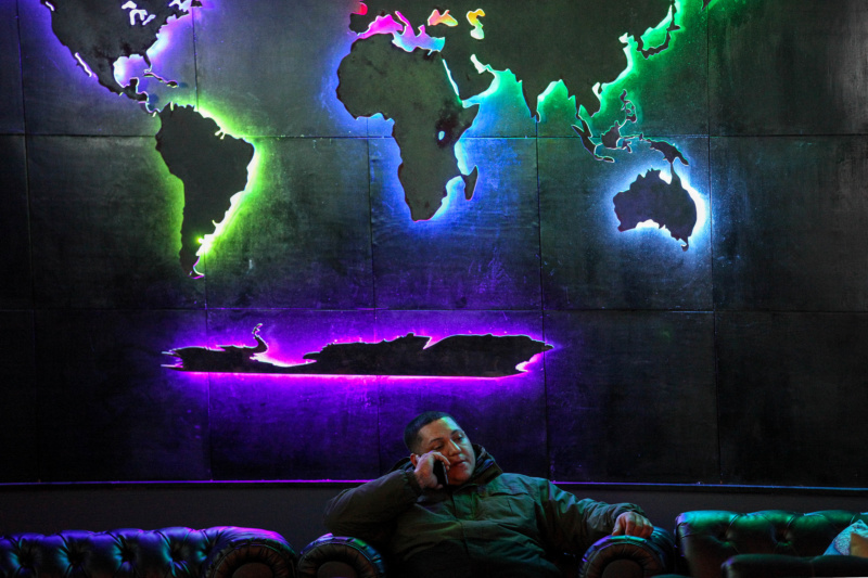 A man sits in Orbis Lounge, under a backlit wall display showing each continent in a world map.