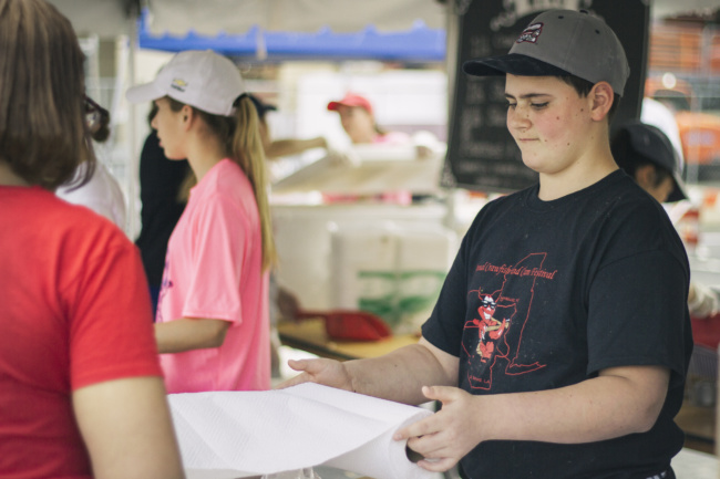 A young teen rolls out paper towels as he helps serve customers.