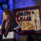 Comedian Michelle Wolf holds a microphone and does a comedy sketch on a stage.
