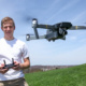 Chase Guttman stands to the left, holding a controler in his hands. A drone hovers in front of him while he controls it.