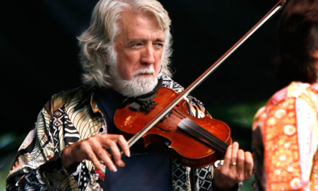 Musician John McEuen holds a fiddle / violin during a performance.