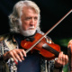 Musician John McEuen holds a fiddle / violin during a performance.