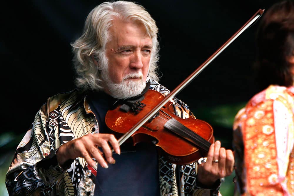 Musician John McEuen holds a fiddle / violin during a performance.