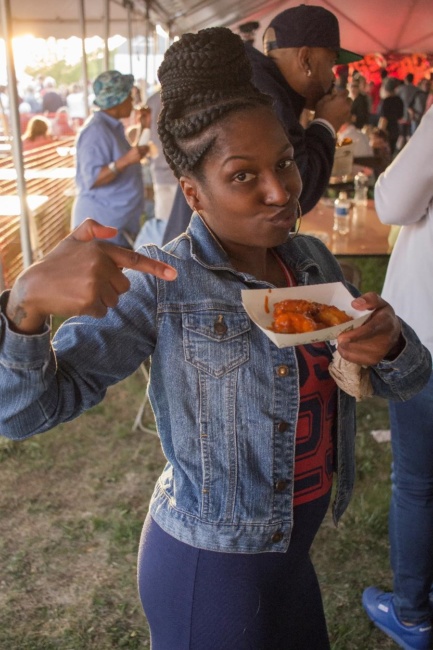 A young woman points excitedly at her plate of chicken wings, dripping in hot sauce, at Wing Fest 2018