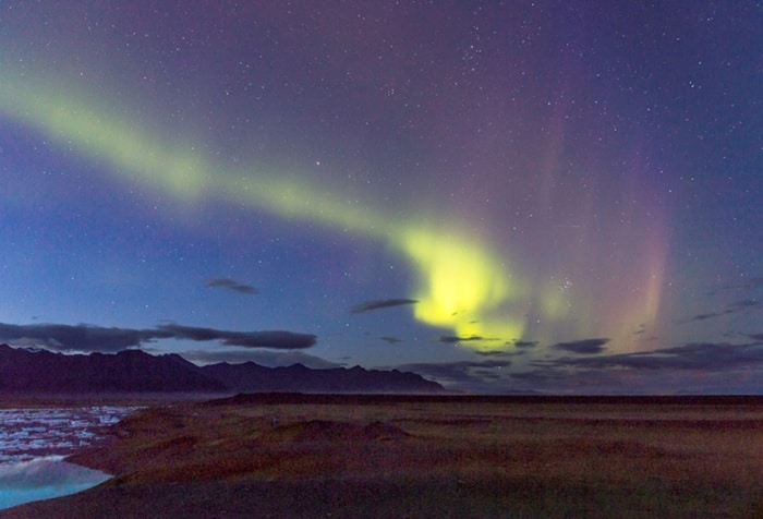 A deep purple sky with yellow Northern Lights over a grassy plane.