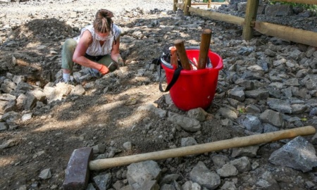 A woman is kneeling on the rocky round, next to a red pail, searching the stones for loose quartz at the Herkimer Diamond Mines.