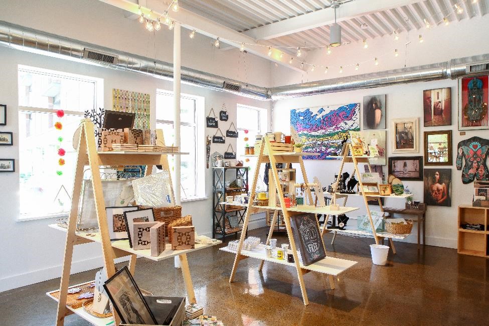 Crafts by local artisans sit on wooden shelves in the center of a room, while prints and fine art -- also made locally -- hang on the shelves.