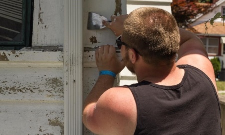 A volunteer scrapes old paint off a home in Syracuse as part of a Workcamp.