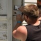 A volunteer scrapes old paint off a home in Syracuse as part of a Workcamp.