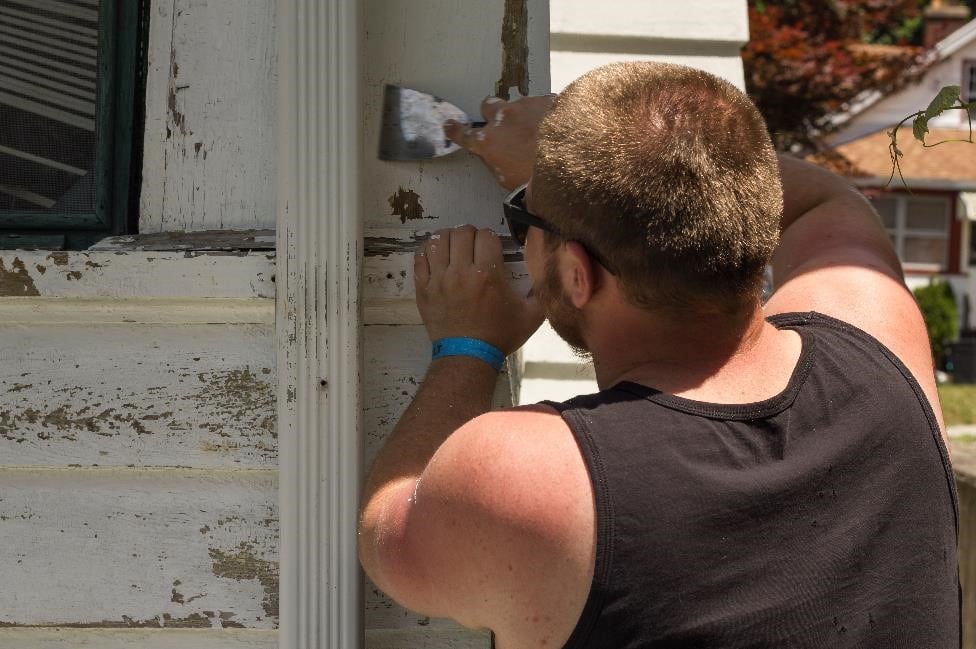 A volunteer scrapes old paint off a home in Syracuse as part of a Workcamp.