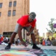 A man bends over with a piece of chalk in hand, surveying his canvas during Street Painting.