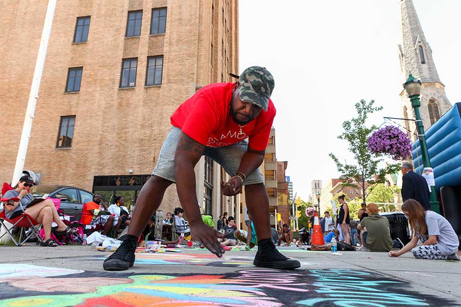 A man bends over with a piece of chalk in hand, surveying his canvas during Street Painting.